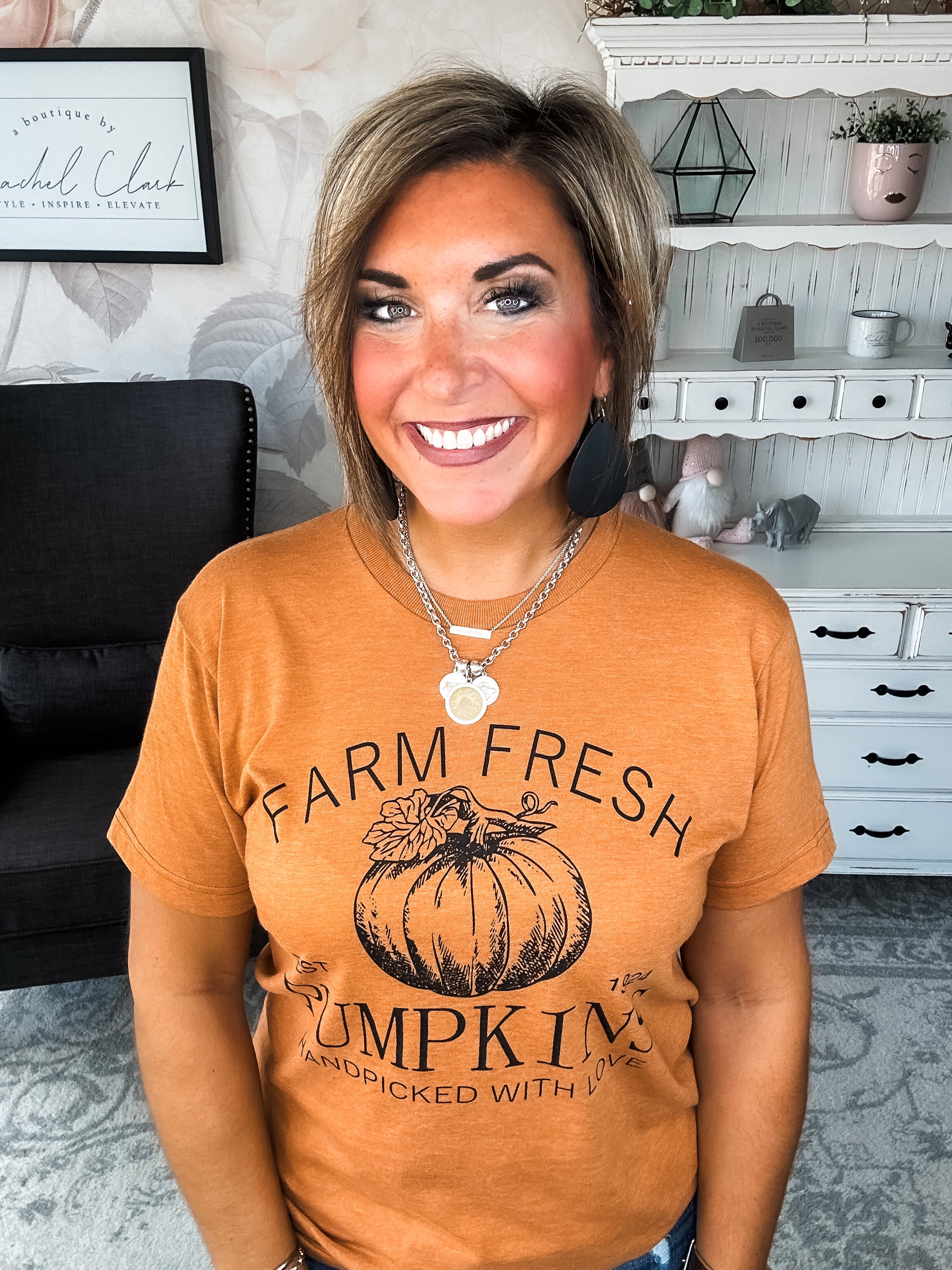 Woman wearing an orange t-shirt that says 'Farm Fresh Pumpkins, Handpicked with Love, Est. 1924' with a pumpkin graphic.