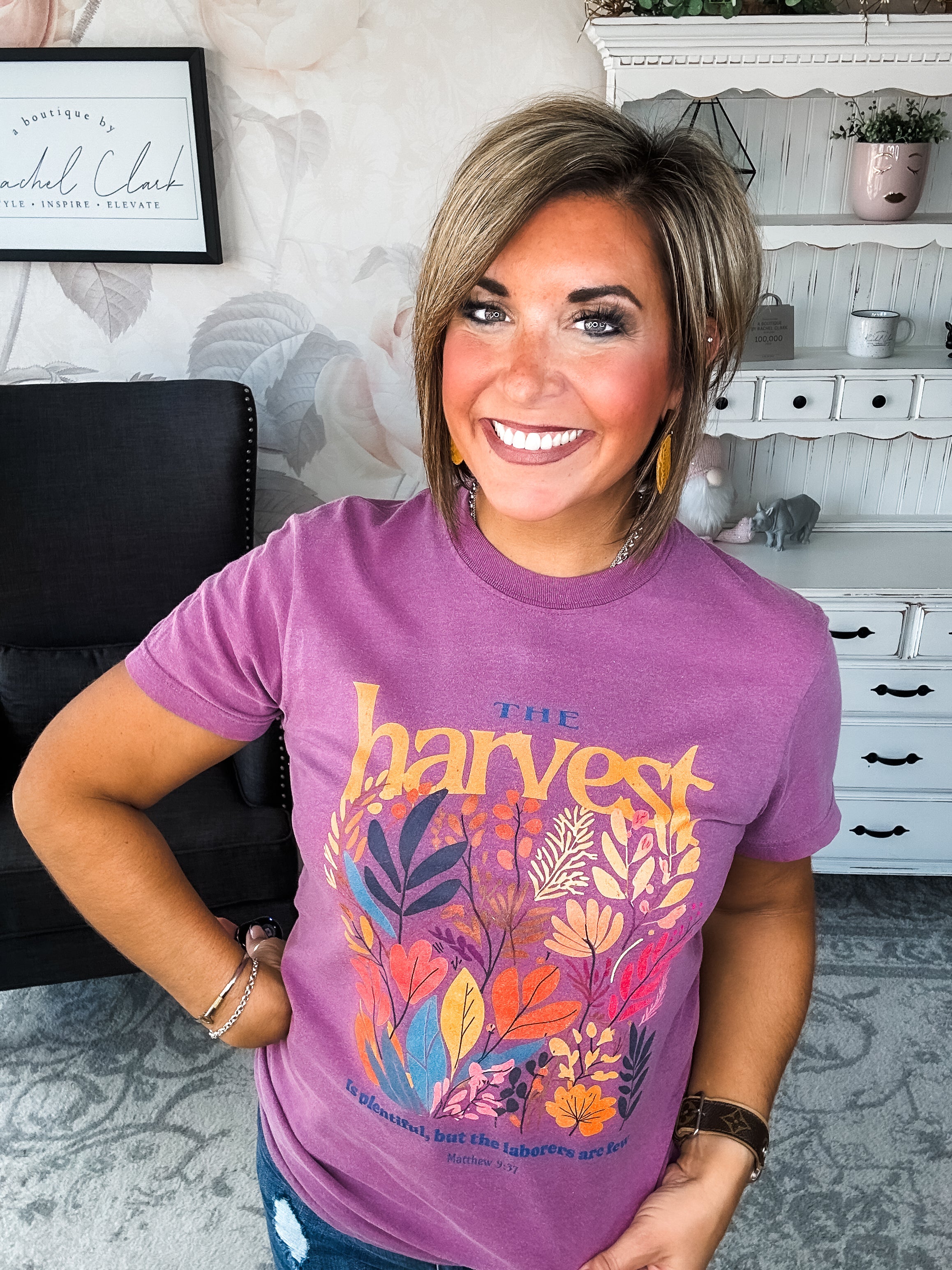 Woman wearing a purple t-shirt with floral designs that reads 'The Harvest is Plentiful, but the Laborers are Few, Matthew 9:37'