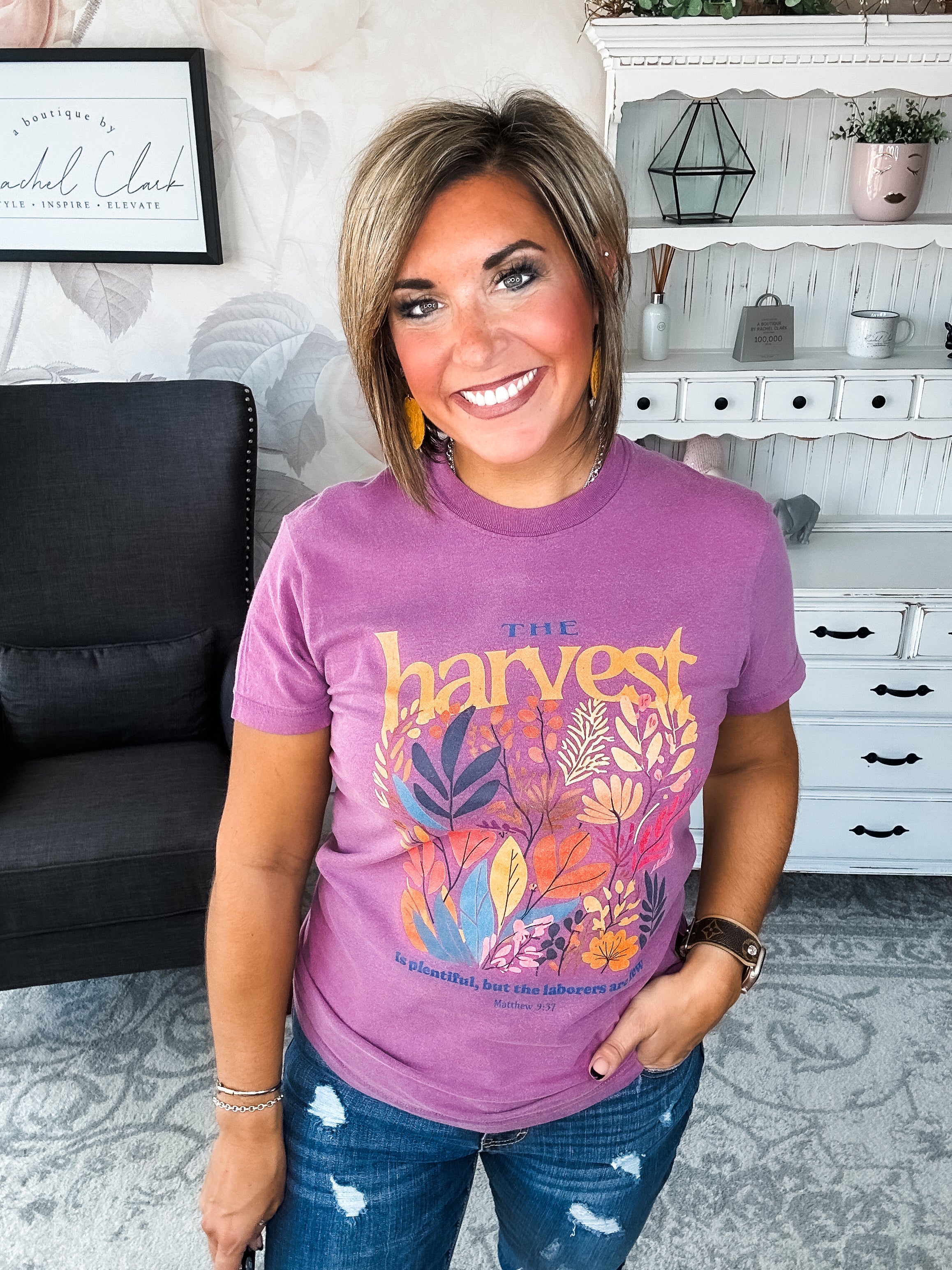 Woman wearing a purple t-shirt with floral designs that reads 'The Harvest is Plentiful, but the Laborers are Few, Matthew 9:37'