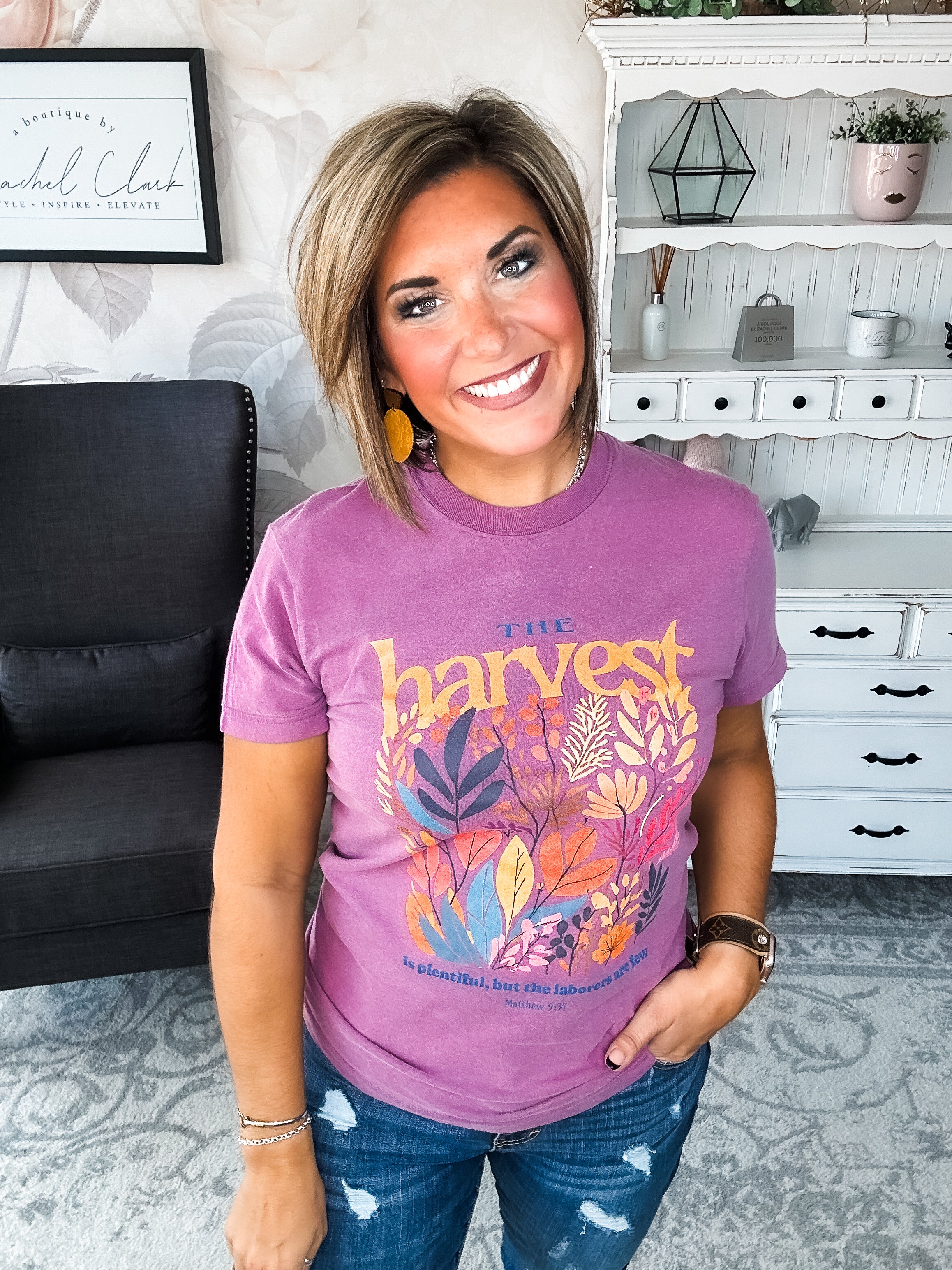 Woman wearing a purple t-shirt with floral designs that reads 'The Harvest is Plentiful, but the Laborers are Few, Matthew 9:37'
