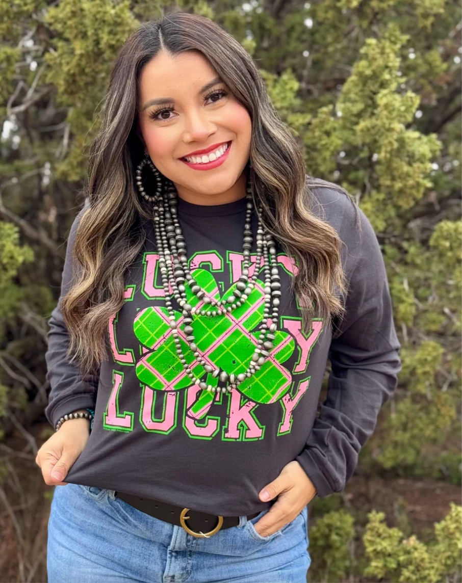 A person wearing a dark grey graphic tee with a color combination of pink, green, and white ink plaid, that reads 'Lucky Lucky Lucky'